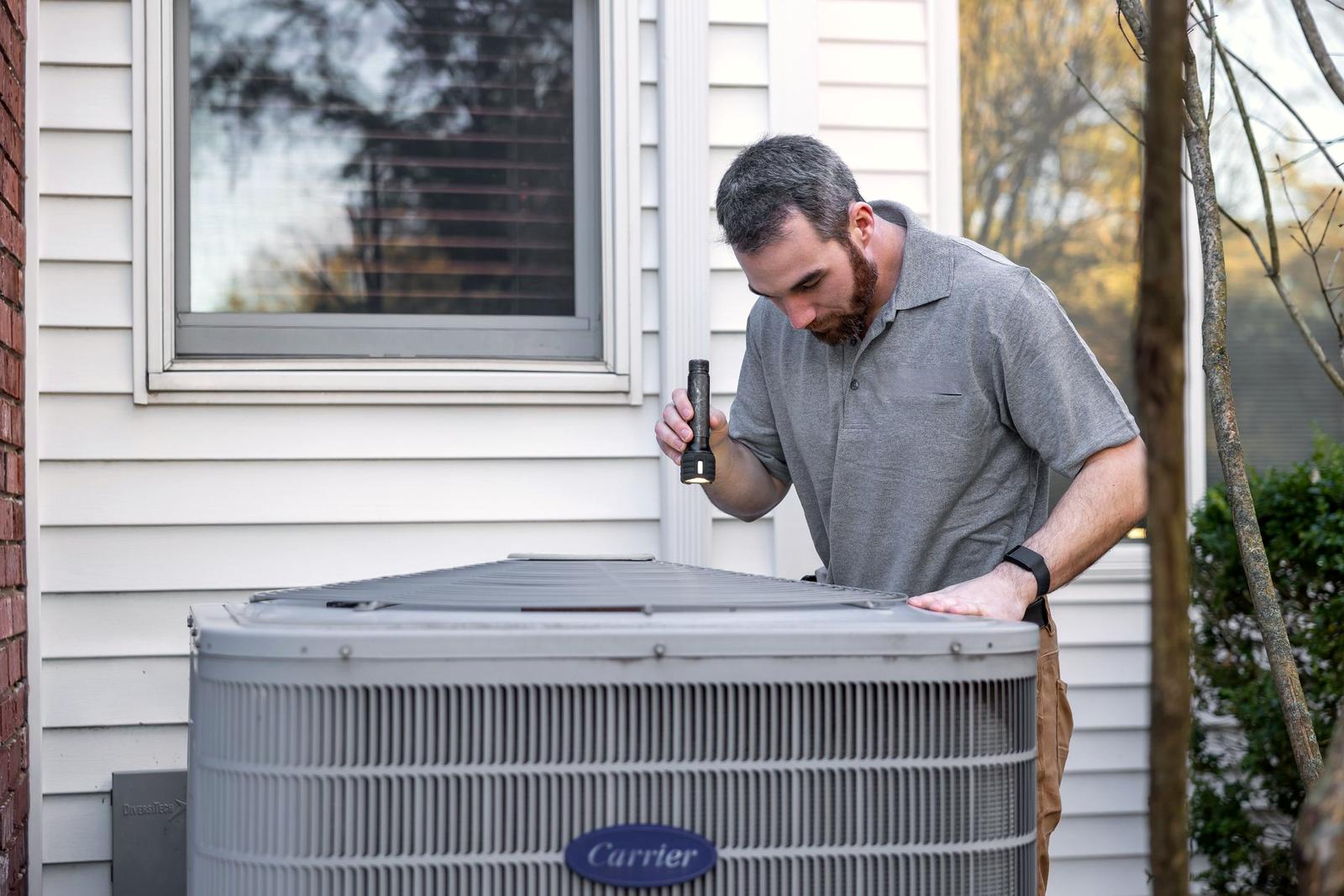 An HVAC technician inspecting an outdoor condenser (stock photo)